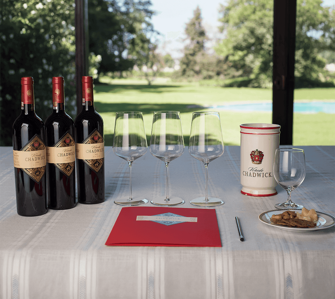 A tasting table set with three bottles of Viñedo Chadwick, looking out onto the garden of the Estate House